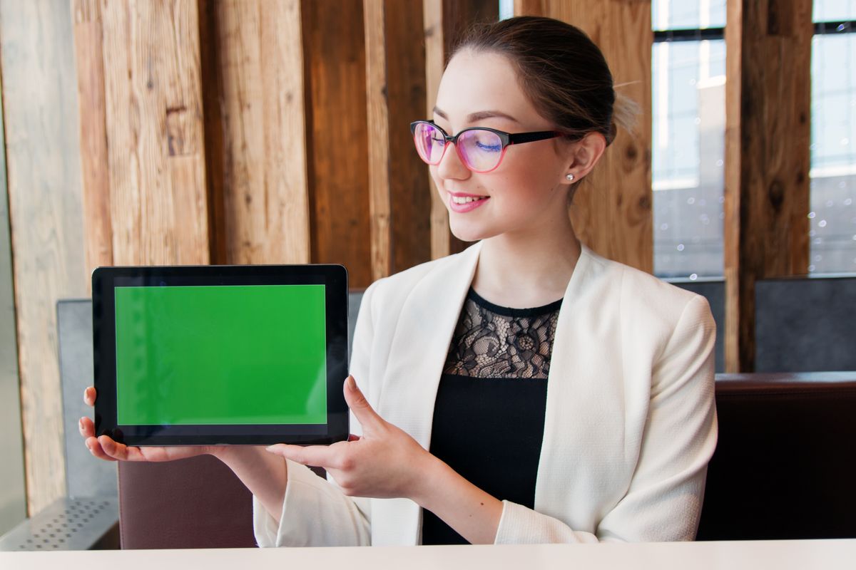 Smiling woman in corporate attire holding a tablet with a green screen indoors