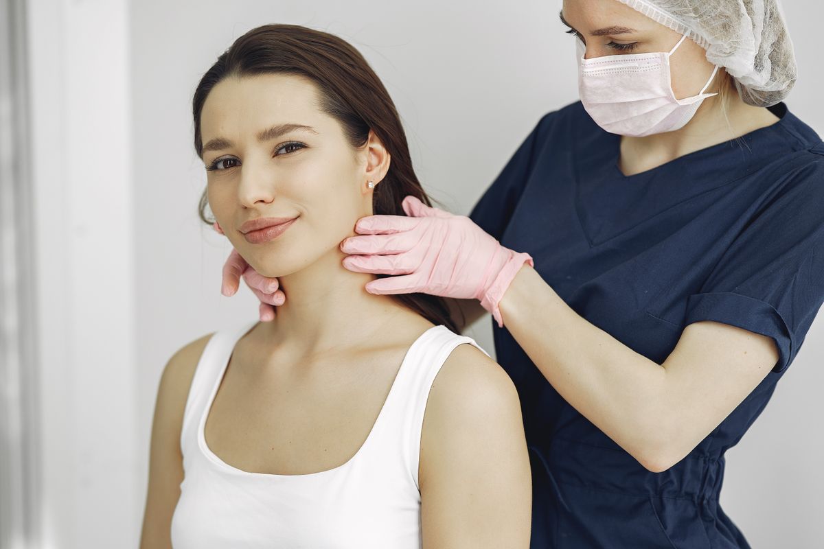 A medical practitioner in scrub suit performs a neck examination