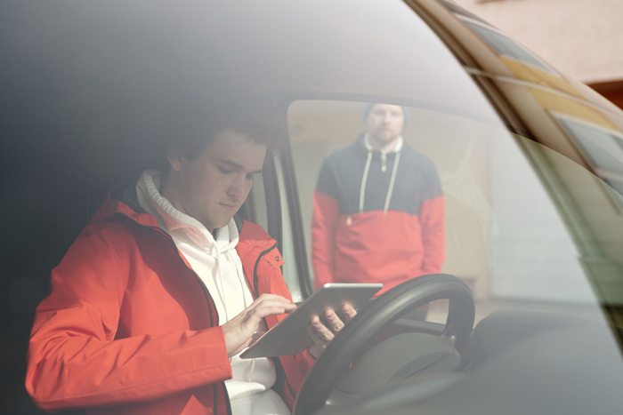 Young man in orange jacket using smartphone inside a car