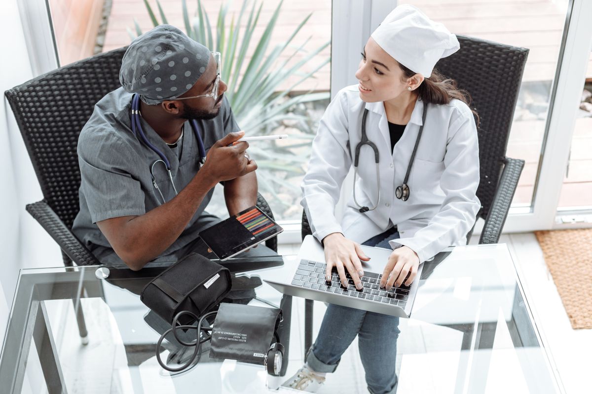 Two doctors discussing patient care using a laptop and tablet indoors
