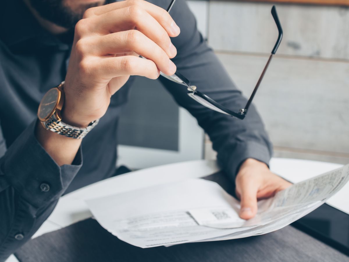 Man in formal attire reviewing paperwork, holding glasses