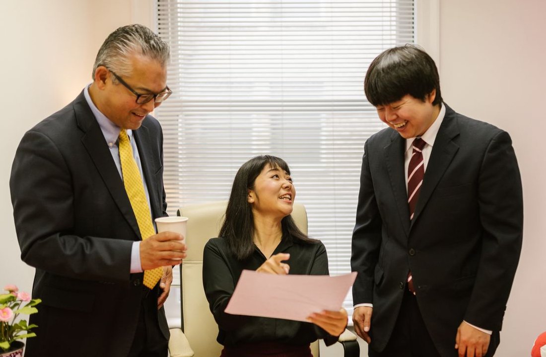 A woman at her desk goes over a document with two smiling colleagues in suits