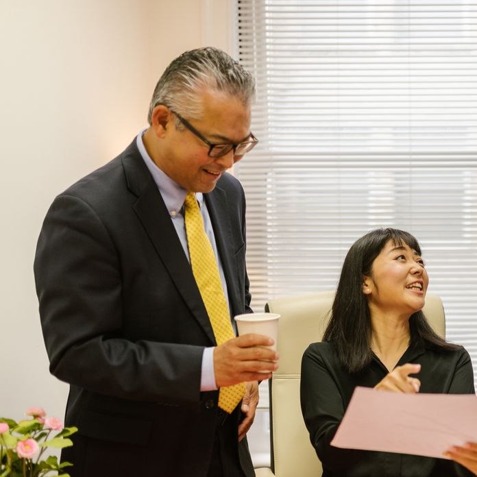 A woman at her desk goes over a document with two smiling colleagues in suits