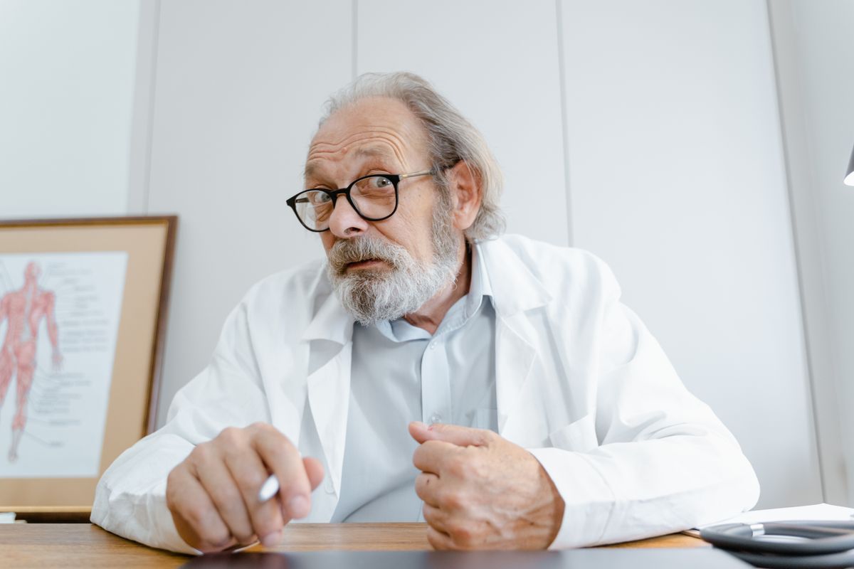 Elderly male doctor in office, wearing glasses, ready for telemedicine session